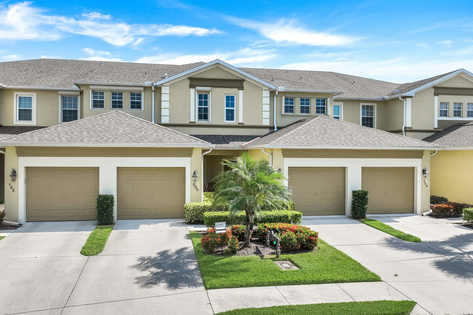 Two-story condominium building at 14712 Calusa Palms Dr, unit 202, with garages, a palm and red flowers in front