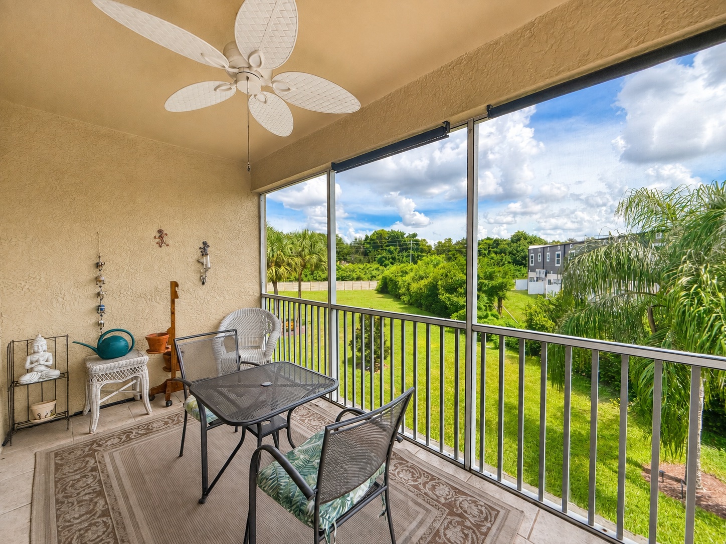 Screened upstairs lanai of unit 204 with ceiling fan, bistro table and a view over green lawn and palm trees